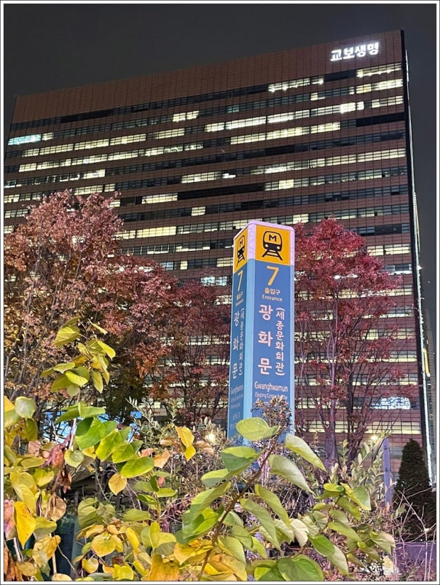 Gwanghwamun Station Exit 7 sign with the illuminated Kyobo Life Insurance building and autumn foliage in downtown Seoul at night