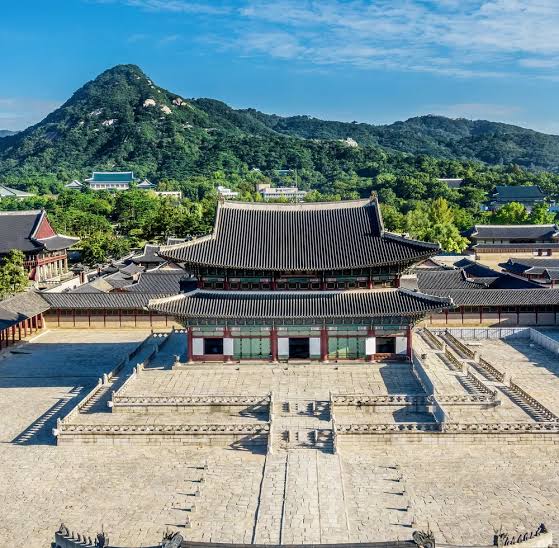 Majestic view of Geunjeongjeon Hall at Gyeongbokgung Palace with Bugaksan Mountain in the background under a blue sky in Seoul