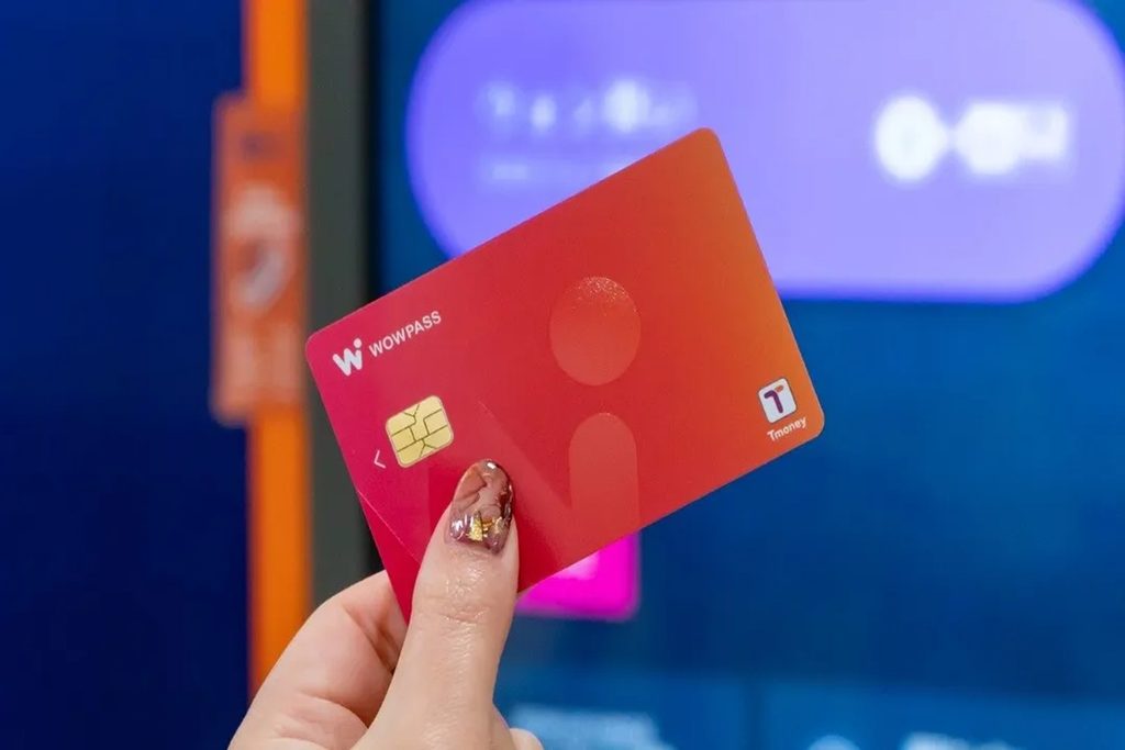 A traveler holding a WOWPASS prepaid debit and T-Money card in front of an automated currency exchange kiosk in Seoul